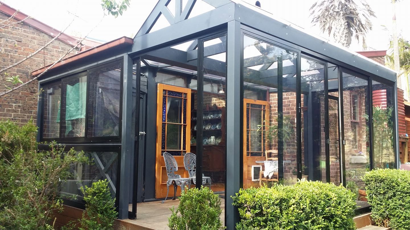 Black framed clear weather screens creating a garden room beside a brick home
