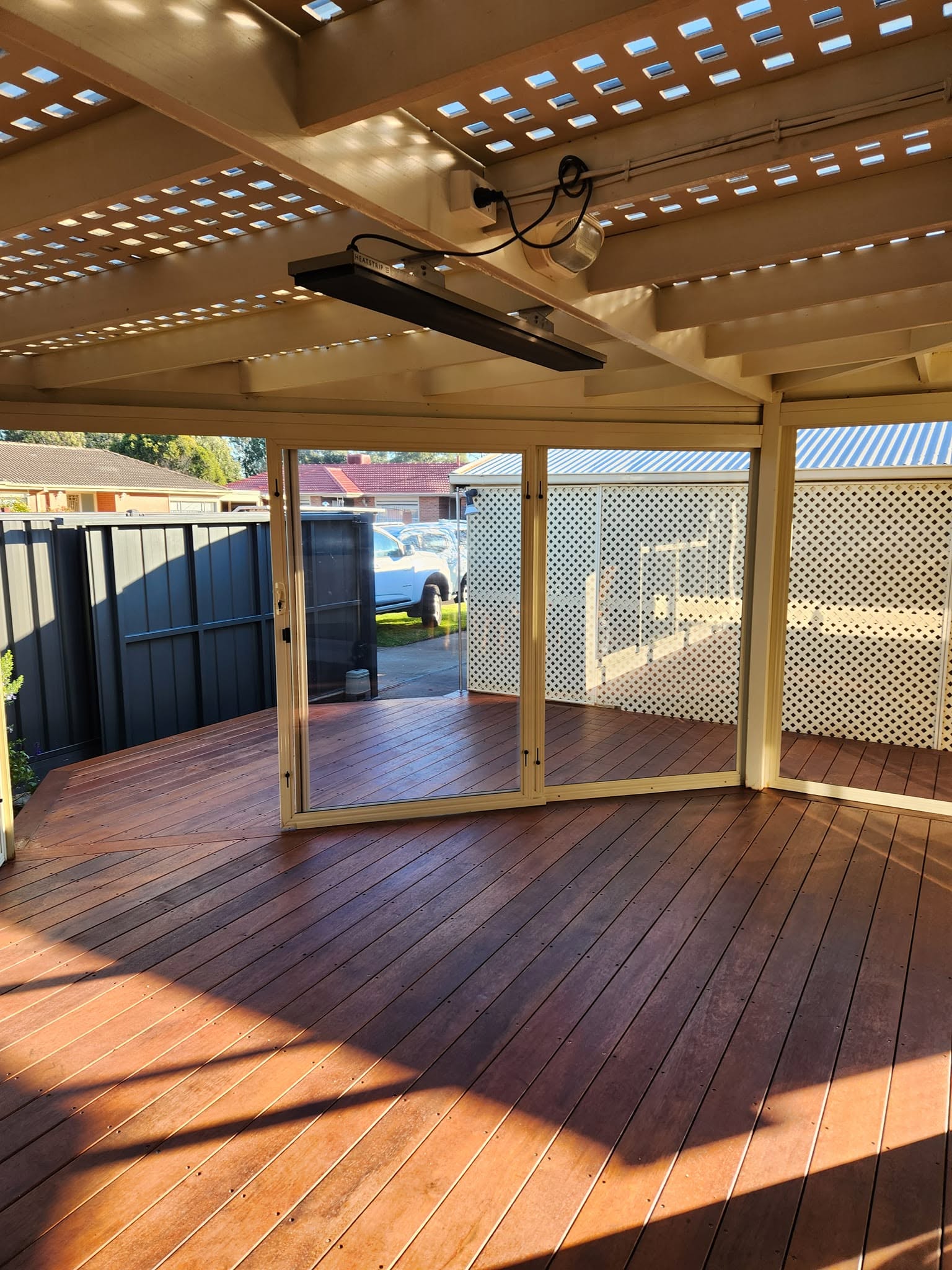 Cream framed weather screens enclosing a sunlit timber veranda