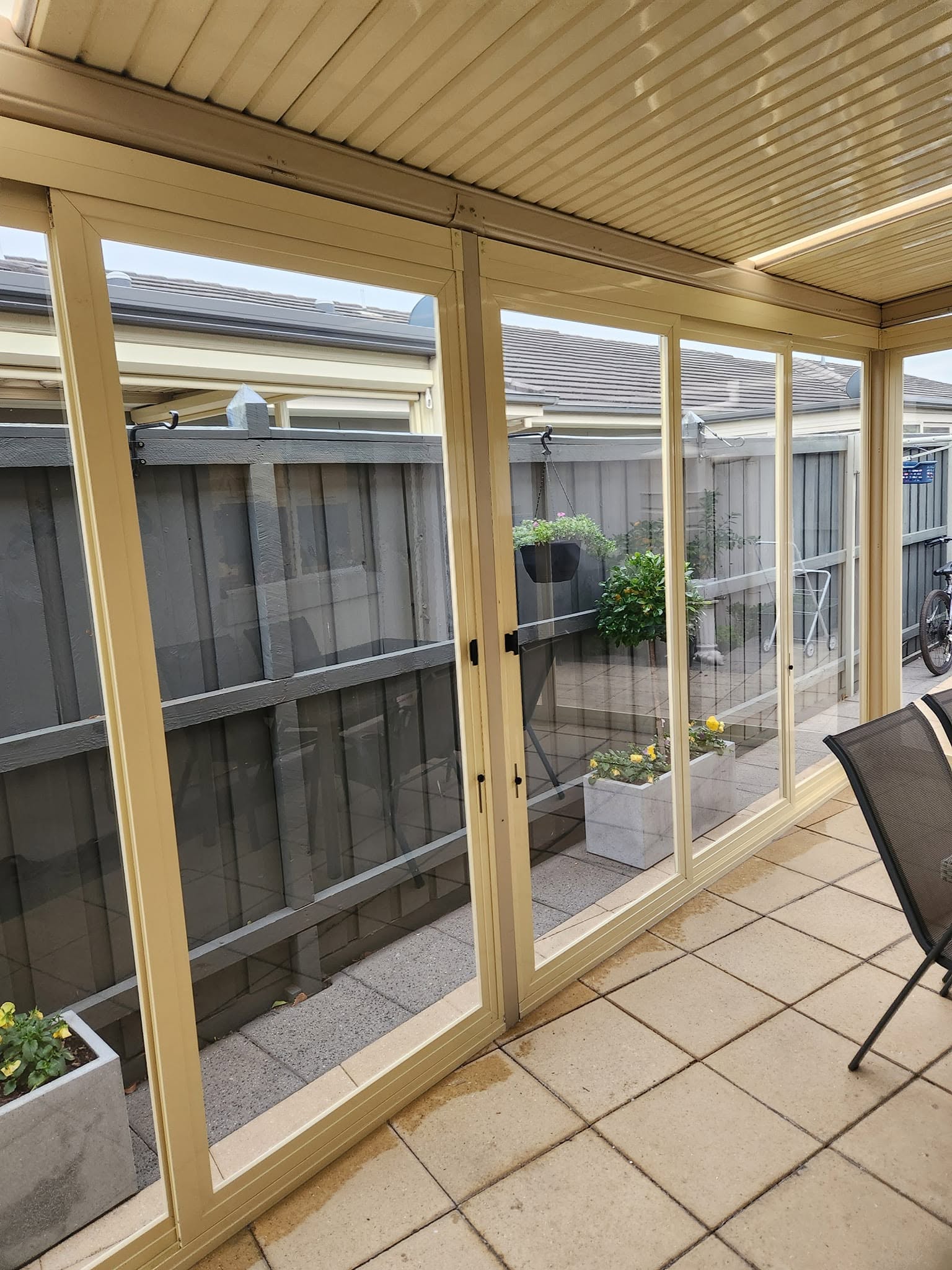 Cream framed clear weather screens enclosing a paved patio